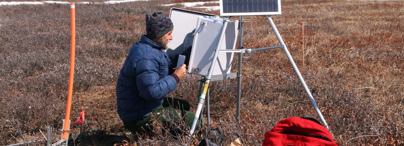 BLM staff setting up data collection equipment on an area in the NPR-A covered in tundra with patches of snow still on the ground.