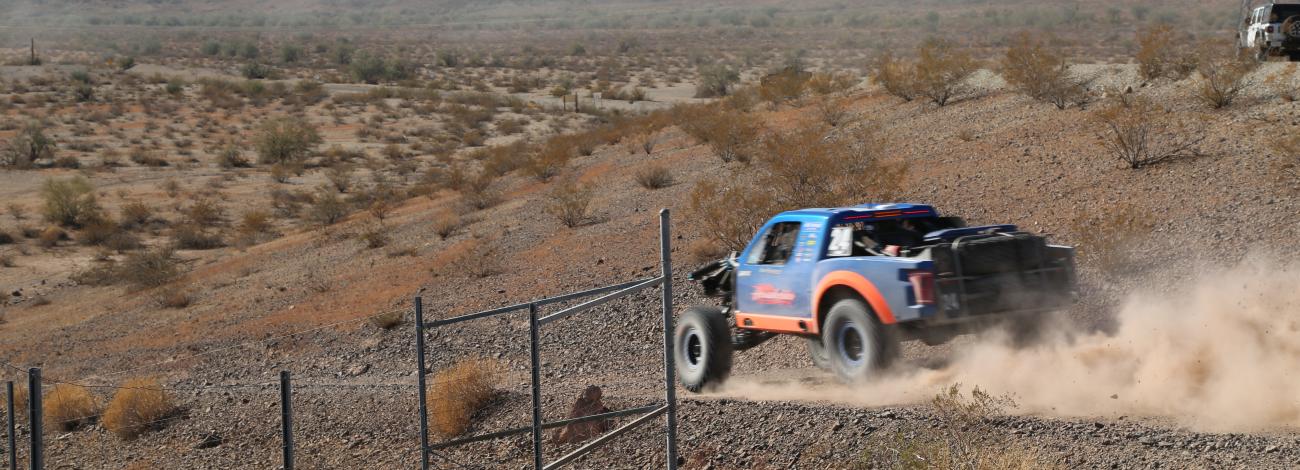 A blue and orange trophy truck speeds through the desert.