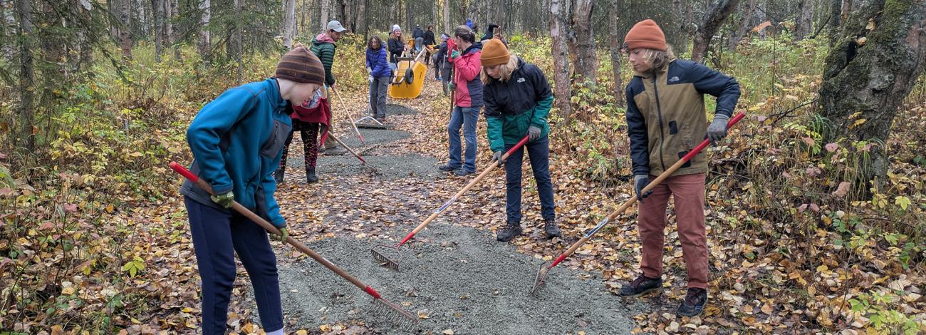 Group of youth volunteers using rakes to spread gravel on a trail at a National Public Lands Day event on Campbell Tract in Alaska.