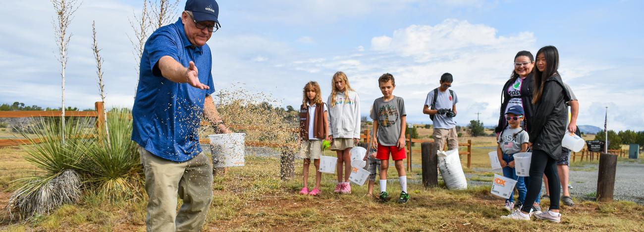 BLM staff show how to plant seeds to a group of kids holding buckets at a National Public Lands Day event in New Mexico in 2024.