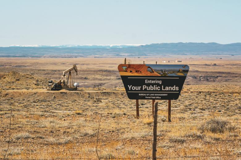 A sign that says "Entering Your Public Lands" In the foreground with an oil derrick in the background on BLM lands