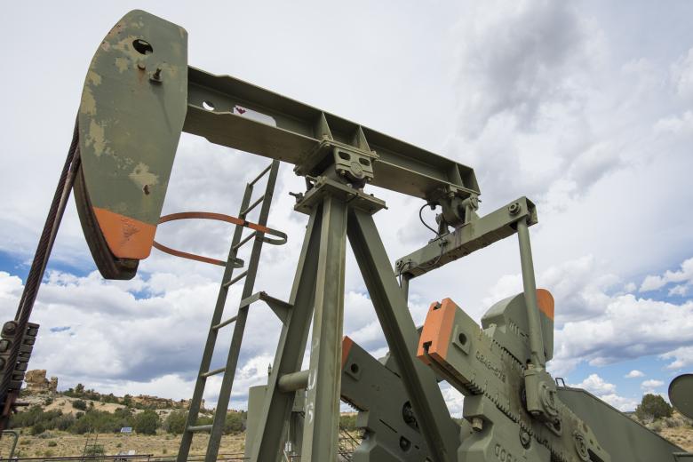 An oil pump jack that's painted green with orange trim is seen with a cloudy sky in the background.