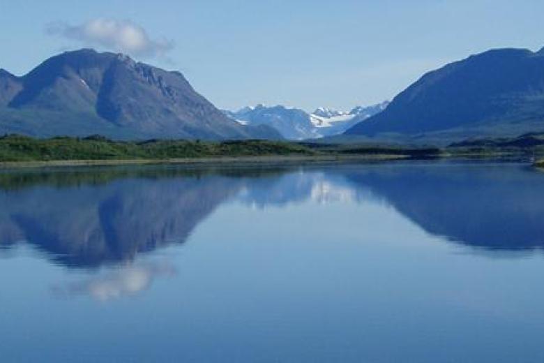 A scenic view of a large lake with mountains and blue sky in the background.