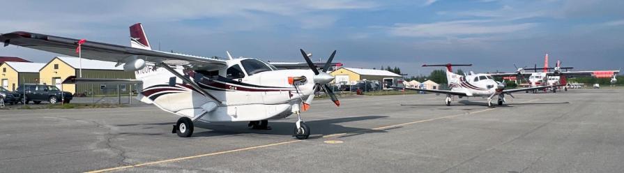 Small airplanes parked on an asphalt ramp. They are mostly white with red stripes.