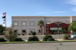 An office building with windows, an asphalt parking lot, and a flag pole flying flags.