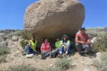 Five interns sitting under a large rock on a grassy surface. 