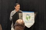 Secretary of the Interior, Deb Haaland, standing at a lectern with a small banner hanging from it which says the Corps Network