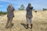 Two researchers observe bank swallows from a distance using binoculars..