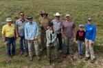 A group of people stand outdoors on grass for a group photo