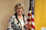 Mona Daniels stands with an award near an american flag indoors.