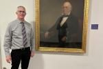 Collin Ewing poses next to a photo of his great-great-great-great-great uncle Thomas Ewing Sr., the first Secretary of the Interior, in the hallway of the Main Interior Building in D.C.