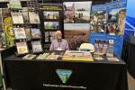 Person sitting at an expo booth surrounded by pamphlets and informational displays