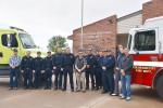 Firefighters in uniform stand in front of two large fire trucks one is green the other is red
