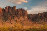 Tall saguaro cactus stands in the foreground of a rugged desert mountain range bathed in warm sunset light.