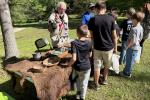 A student stands at an outdoor table that is covered in animal pelts and archeological artifacts