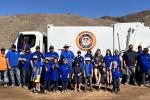 A Yuma County Public Works truck and a large roll-off dumpster sit in a desert cleanup area as volunteers collect trash across rocky public lands near Yuma, Arizona.