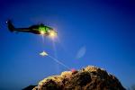 A helicopter hoists a litter from rescuers positioned on a rocky ridge during a nighttime rescue training exercise.