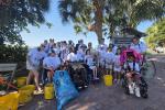 Group of people, including children and individuals in wheelchairs, gathered outdoors near palm trees with recycling buckets and bags.