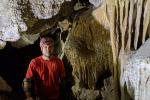 A man sits in a cave next to cave formations. 