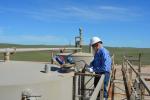a man in a blue shirt and white hard hat inspects an opening in a metal structure